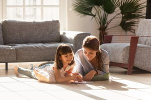 Happy mom helping child girl drawing on warm floor together